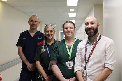A photo of four people standing in a line in a hospital corridor.